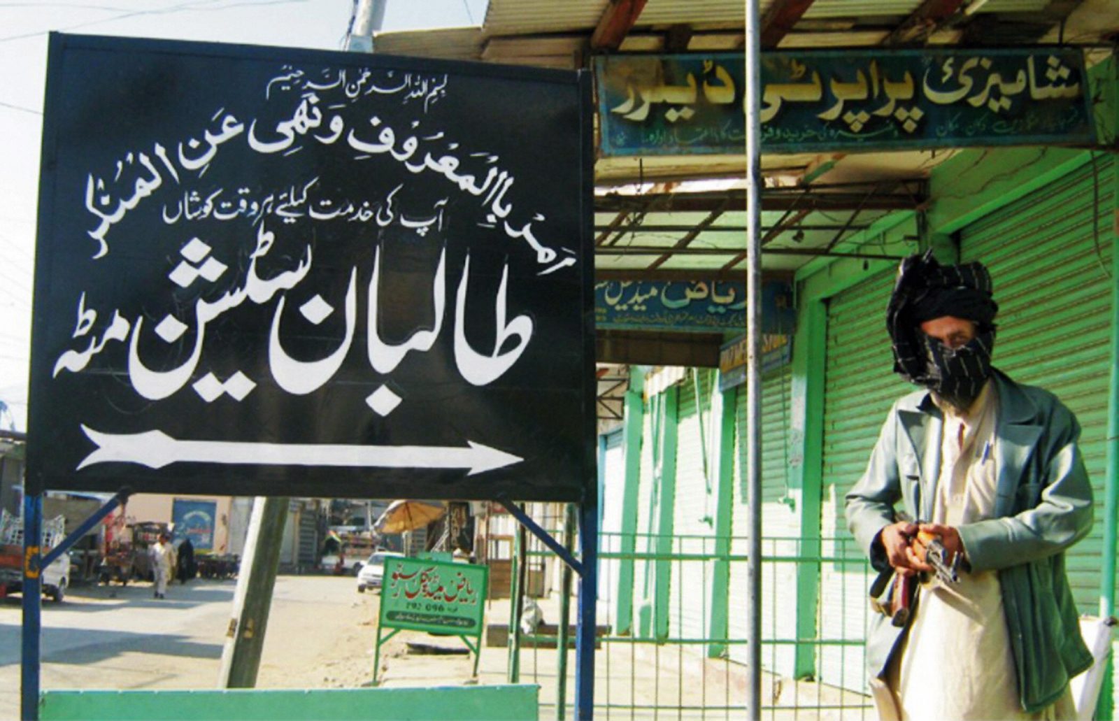 pro-Taliban militant standing by sign reading "Taliban Station"